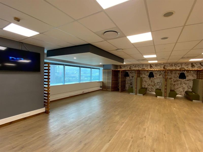 Open-plan office space featuring wood-look flooring, suspended acoustic ceiling tiles, recessed lighting, and large windows providing natural light and city views.