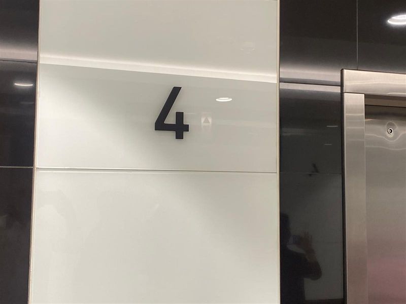 A modern office building elevator lobby area featuring high-gloss wall paneling and stainless steel elevator doors on the fourth floor.