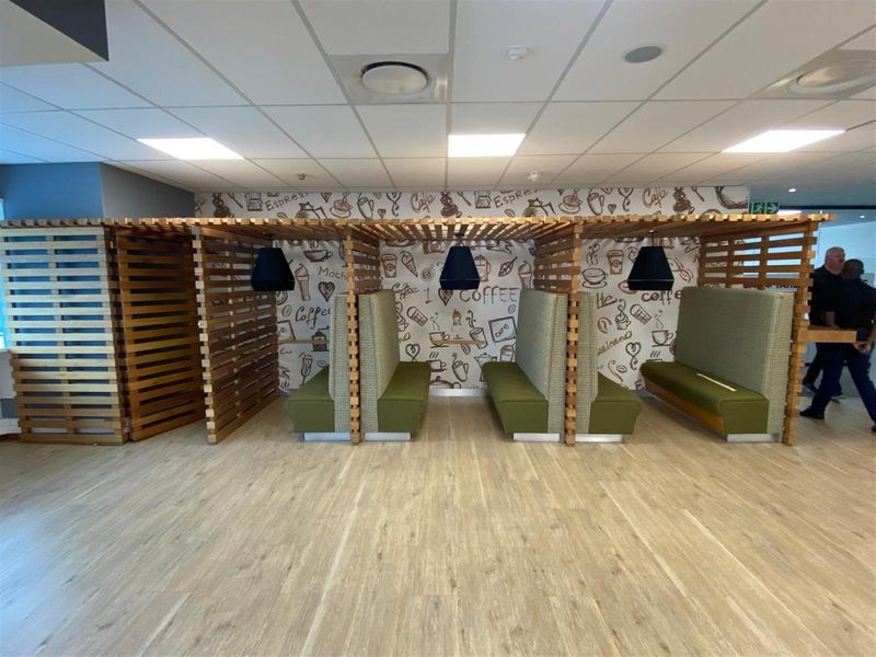 Modern office breakout area featuring built-in wooden slatted privacy booths with integrated seating and pendant lighting against a decorative coffee-themed feature wall.