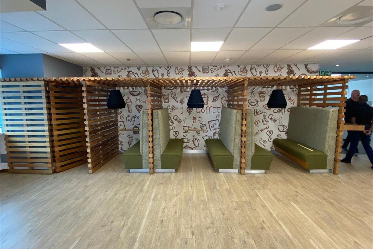 Modern office breakout area featuring built-in wooden slatted privacy booths with integrated seating and pendant lighting against a decorative coffee-themed feature wall.
