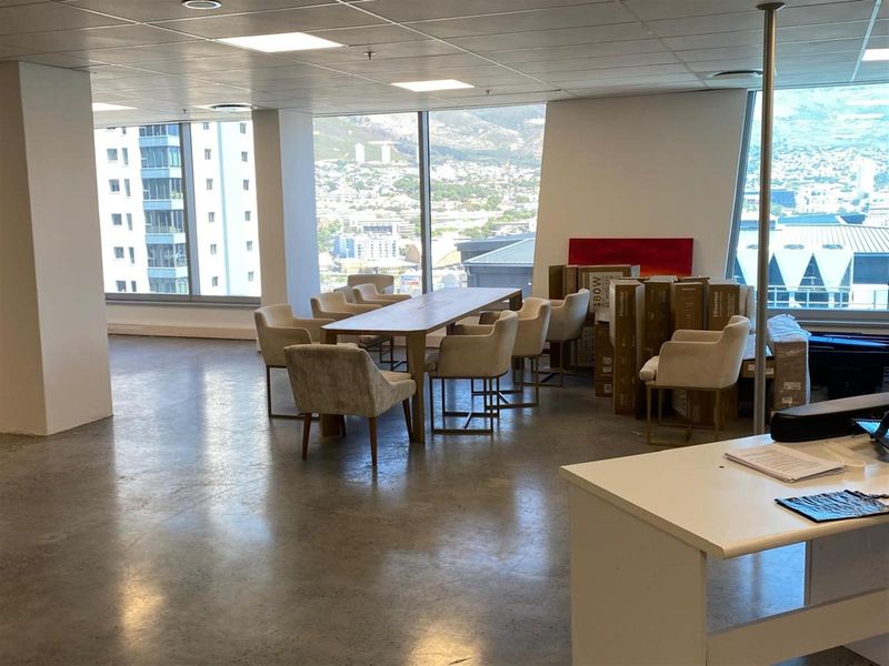 Spacious open-plan office area featuring polished concrete flooring, recessed ceiling lighting, and expansive floor-to-ceiling windows offering panoramic city and mountain views.