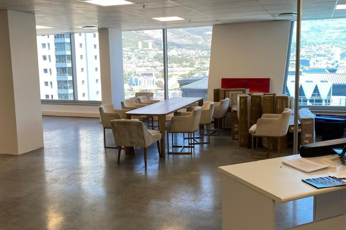 Spacious open-plan office area featuring polished concrete flooring, recessed ceiling lighting, and expansive floor-to-ceiling windows offering panoramic city and mountain views.