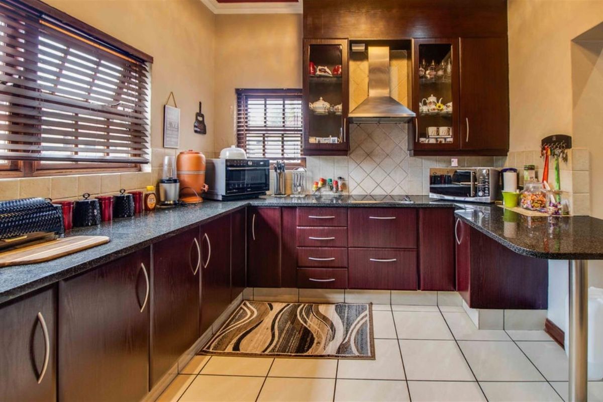 A functional kitchen featuring dark wood cabinetry, granite countertops, tiled flooring, and a stainless steel extractor fan.