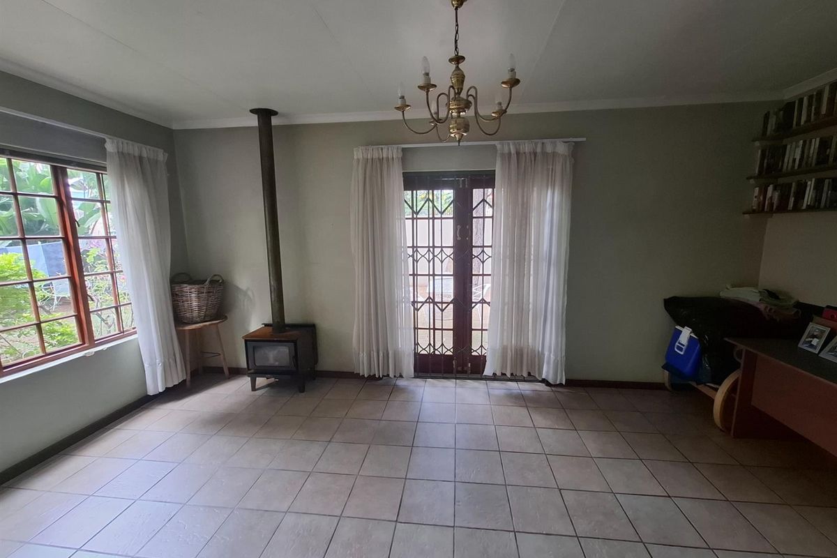 A living room featuring tiled flooring, a built-in wood-burning fireplace, a classic chandelier, and glass-paned doors leading to the exterior.