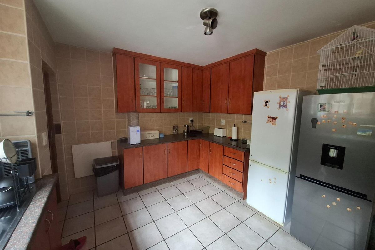 A functional kitchen featuring wooden cabinetry, tiled walls, and tiled flooring, providing a practical workspace with ample storage and counter space.