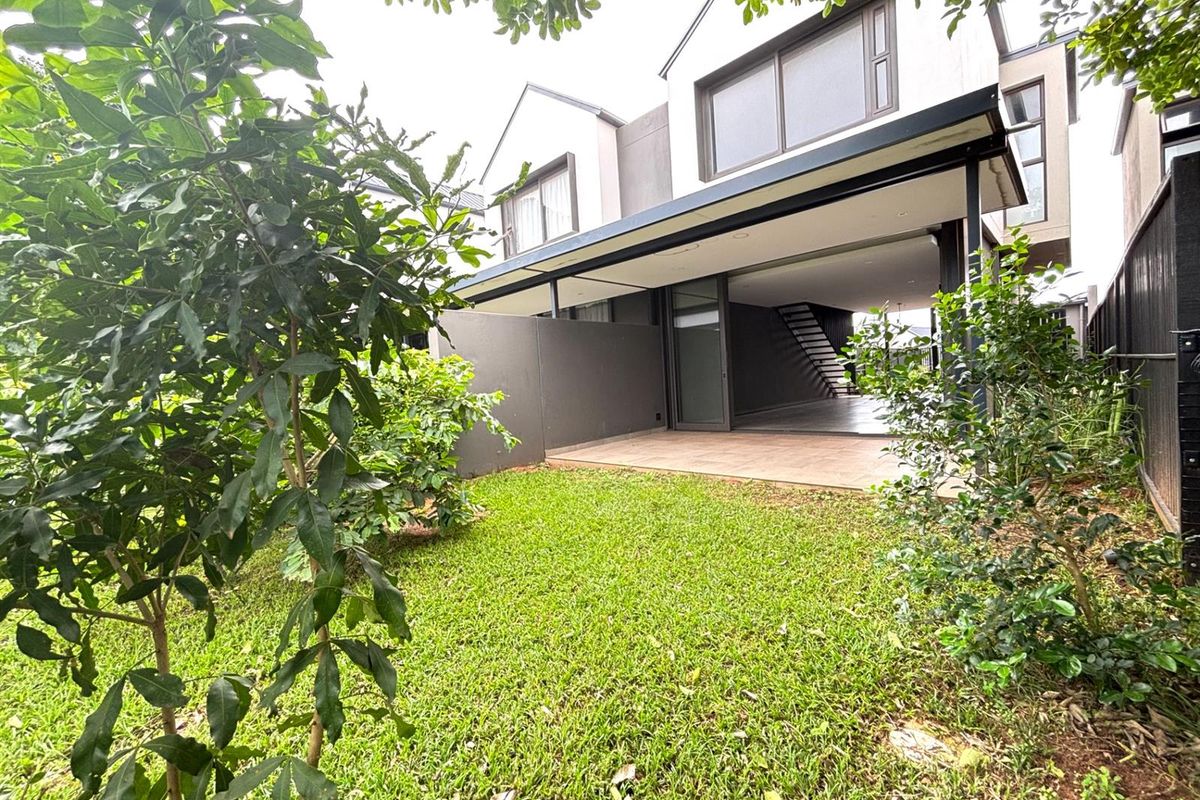 Rear view of the townhouse featuring a covered patio area, landscaped garden, and modern architectural design with large sliding glass doors.