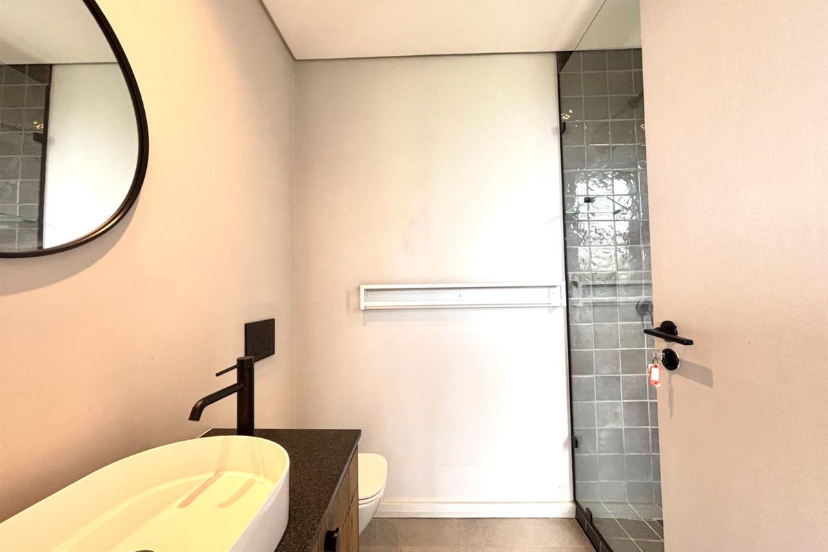Modern bathroom featuring a vessel sink with matte black faucet, vanity cabinet, and a glass-enclosed shower with grey tiled walls.