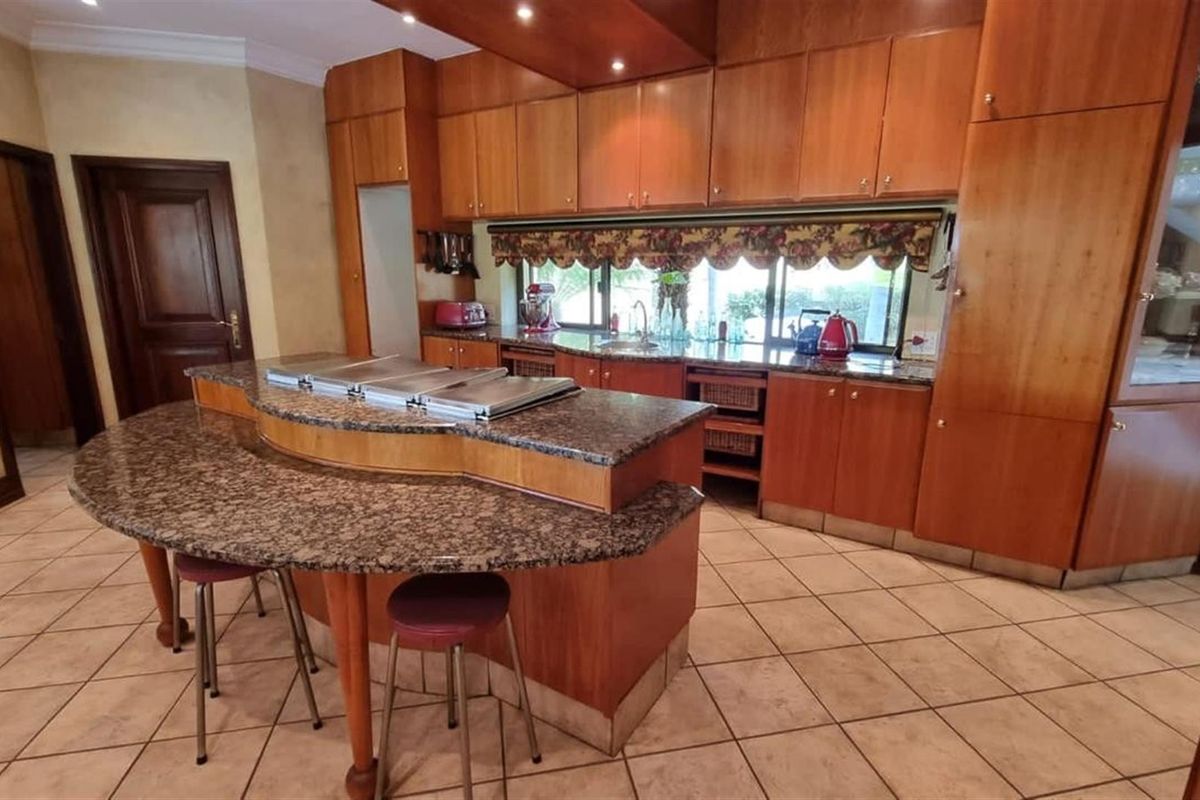 Spacious kitchen featuring extensive wooden cabinetry, granite countertops, a central island with breakfast bar seating, and tiled flooring.