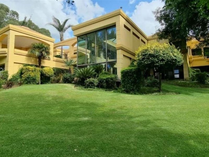 A spacious rear exterior view of a multi-level residence featuring large glass windows, covered balconies, and a well-maintained expansive lawn.
