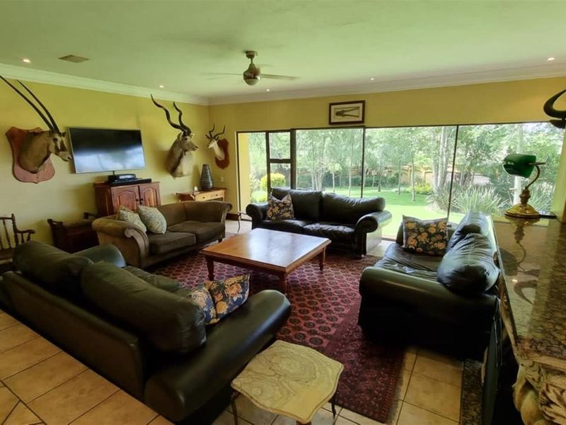 Spacious living room featuring large floor-to-ceiling windows with garden views, tiled flooring, and recessed ceiling lighting.