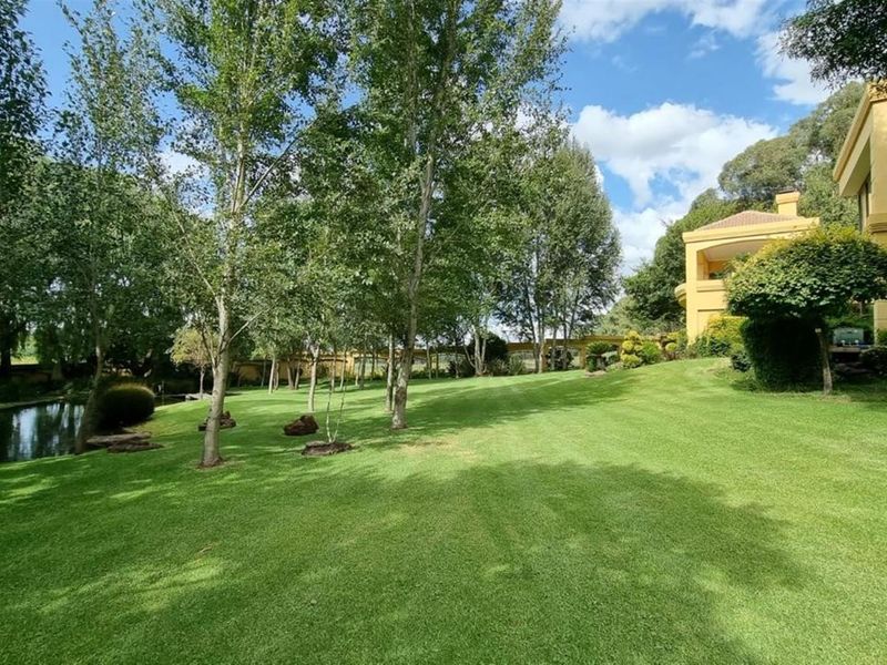 A spacious, well-maintained garden featuring a lush green lawn, mature trees, and a tranquil pond, adjacent to the rear elevation of the house.