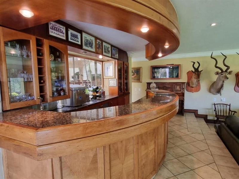 A spacious built-in wooden bar area featuring a curved granite countertop, integrated cabinetry, and recessed lighting, perfect for entertaining.