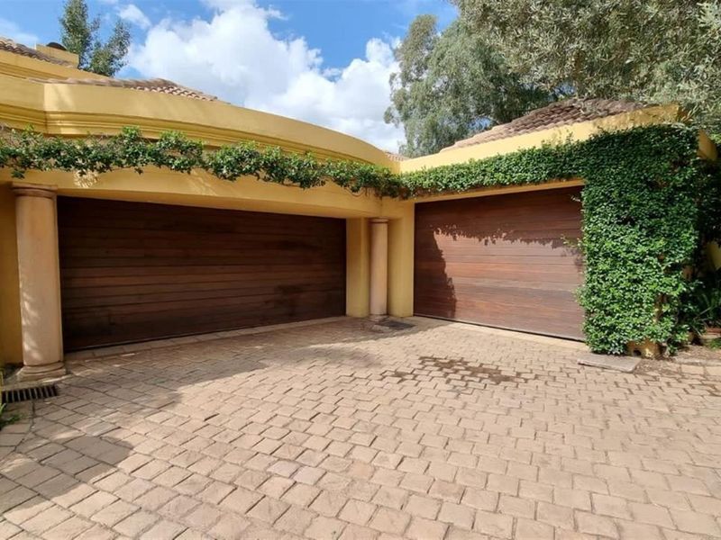 A well-maintained double garage featuring timber sectional doors, stone-paved driveway, and decorative architectural columns with climbing greenery.