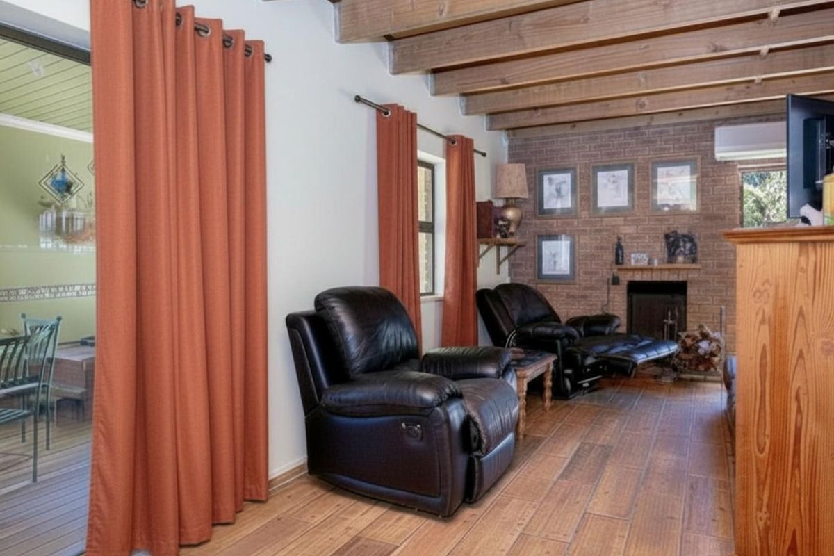A cozy living room featuring exposed timber ceiling beams, a brick fireplace, and wood-look flooring, with direct access to an outdoor patio area.
