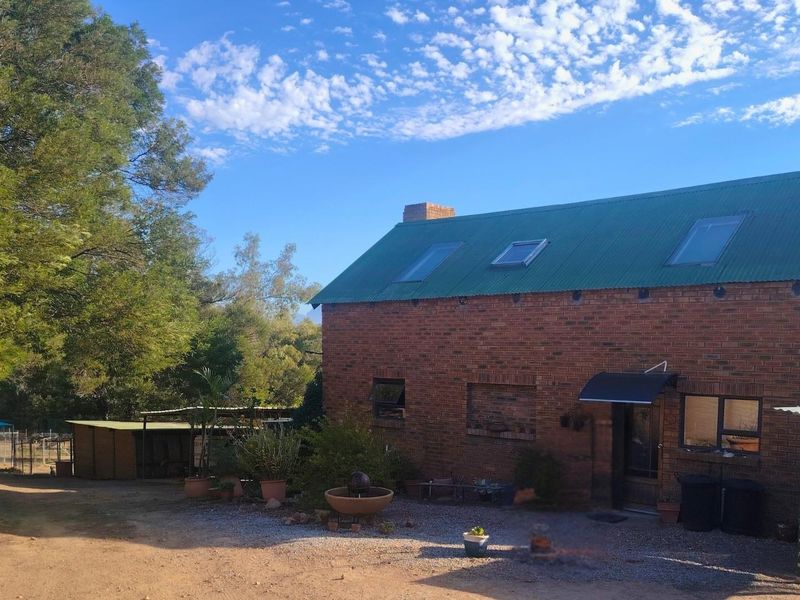 A rustic brick farmhouse featuring a green corrugated metal roof with skylights, set within a spacious rural landscape.
