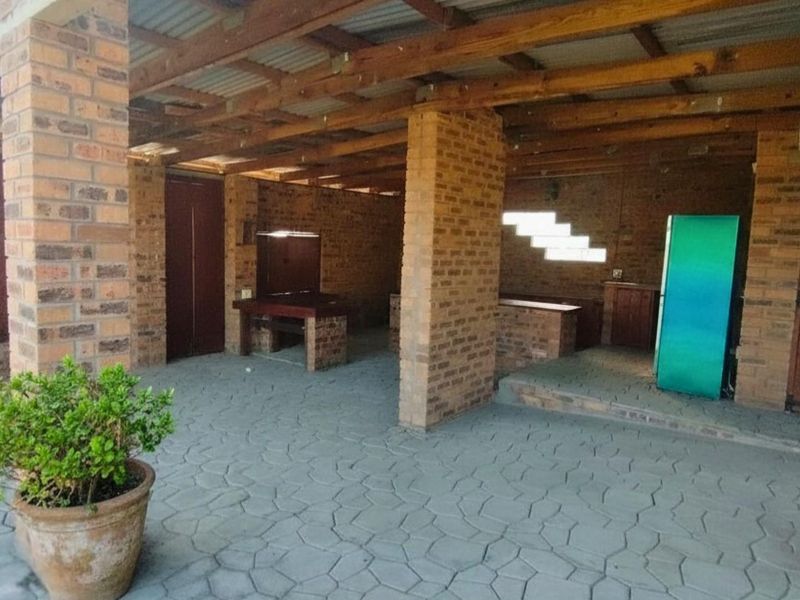A rustic covered outdoor entertainment area featuring exposed brick pillars, timber roof structure, and paved flooring, ideal for farm-style gatherings.