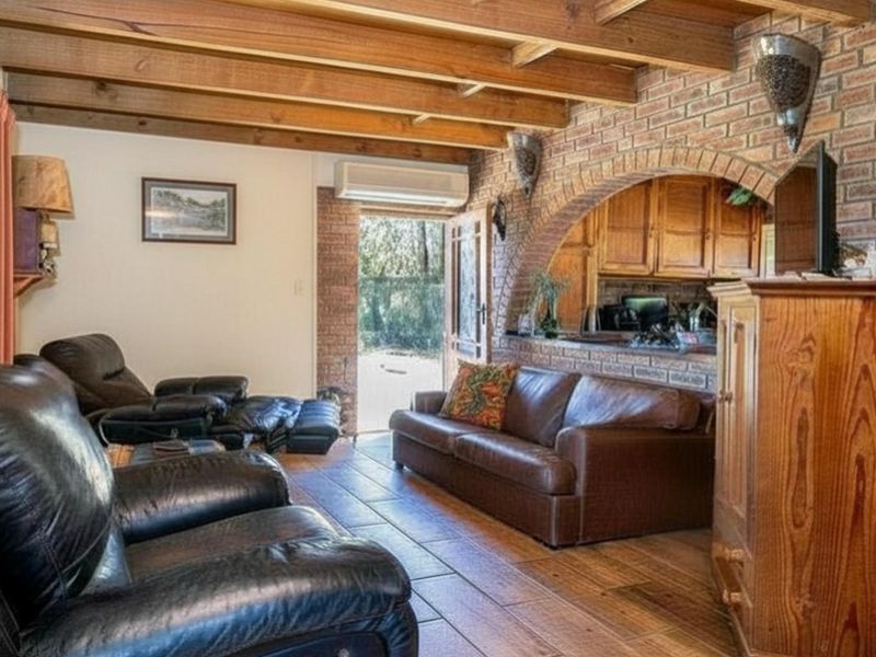 Open plan living area featuring exposed timber ceiling beams, rustic brick feature walls, and a pass-through opening to the kitchen area.