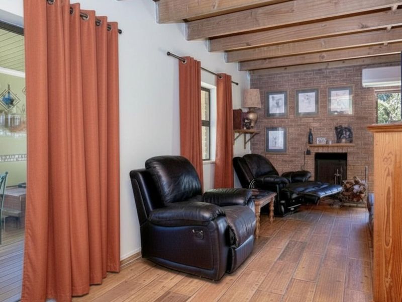 A cozy living room featuring exposed timber ceiling beams, a brick fireplace, and wood-look flooring, with direct access to an outdoor patio area.