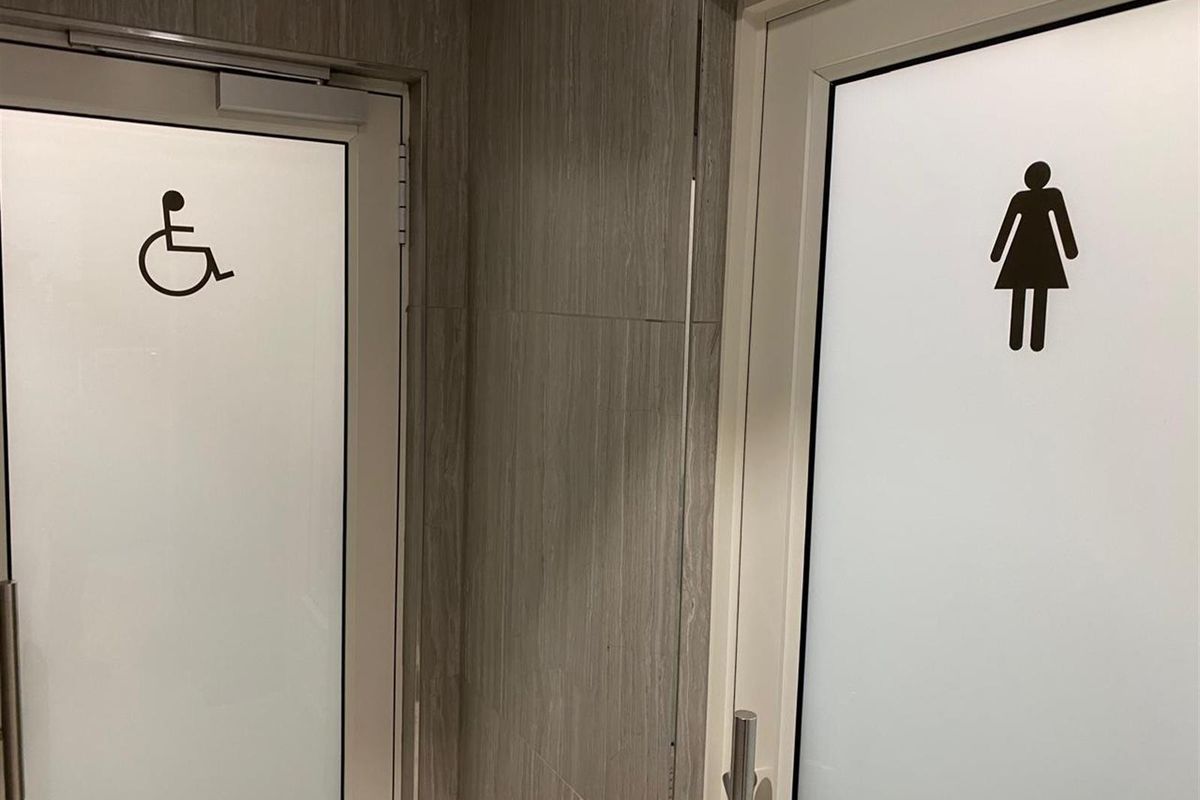A view of two office restroom entrances featuring modern frosted glass doors with clear accessibility and gender signage.