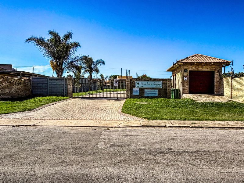 Front entrance view of the residential estate featuring a paved driveway, brick boundary walls, security gate, and a small guardhouse structure.
