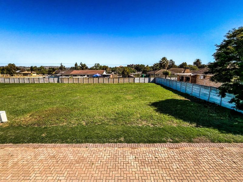 A spacious, level residential vacant plot featuring established lawn, perimeter concrete walling, and a paved foreground area.