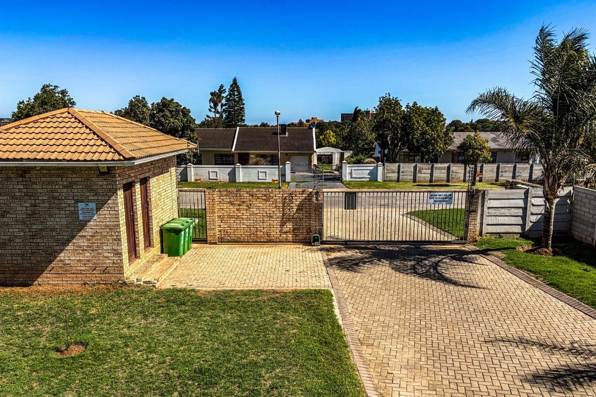 View of the property entrance featuring a brick-built guard house, paved driveway, and secure metal gate access.
