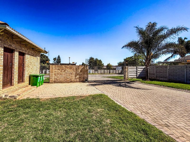 A paved driveway leading to a secure metal gate, featuring brick boundary walls and a well-maintained lawn area.