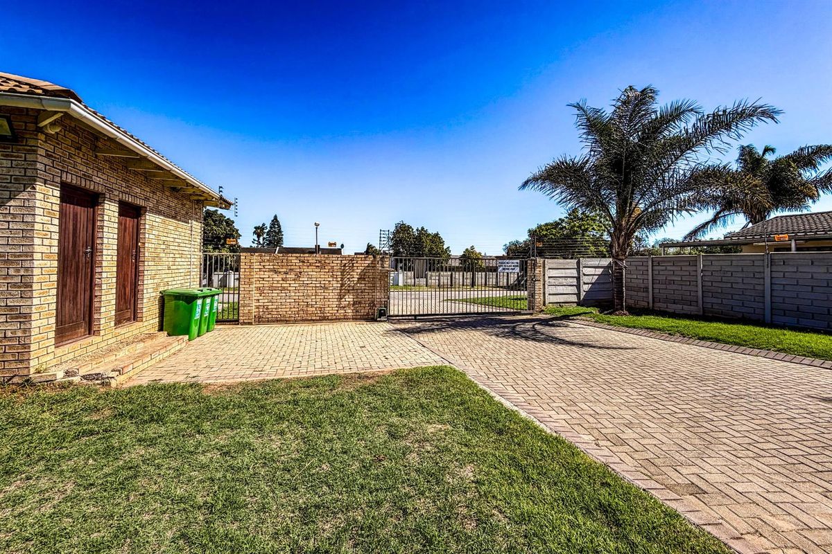 A paved driveway leading to a secure metal gate, featuring brick boundary walls and a well-maintained lawn area.