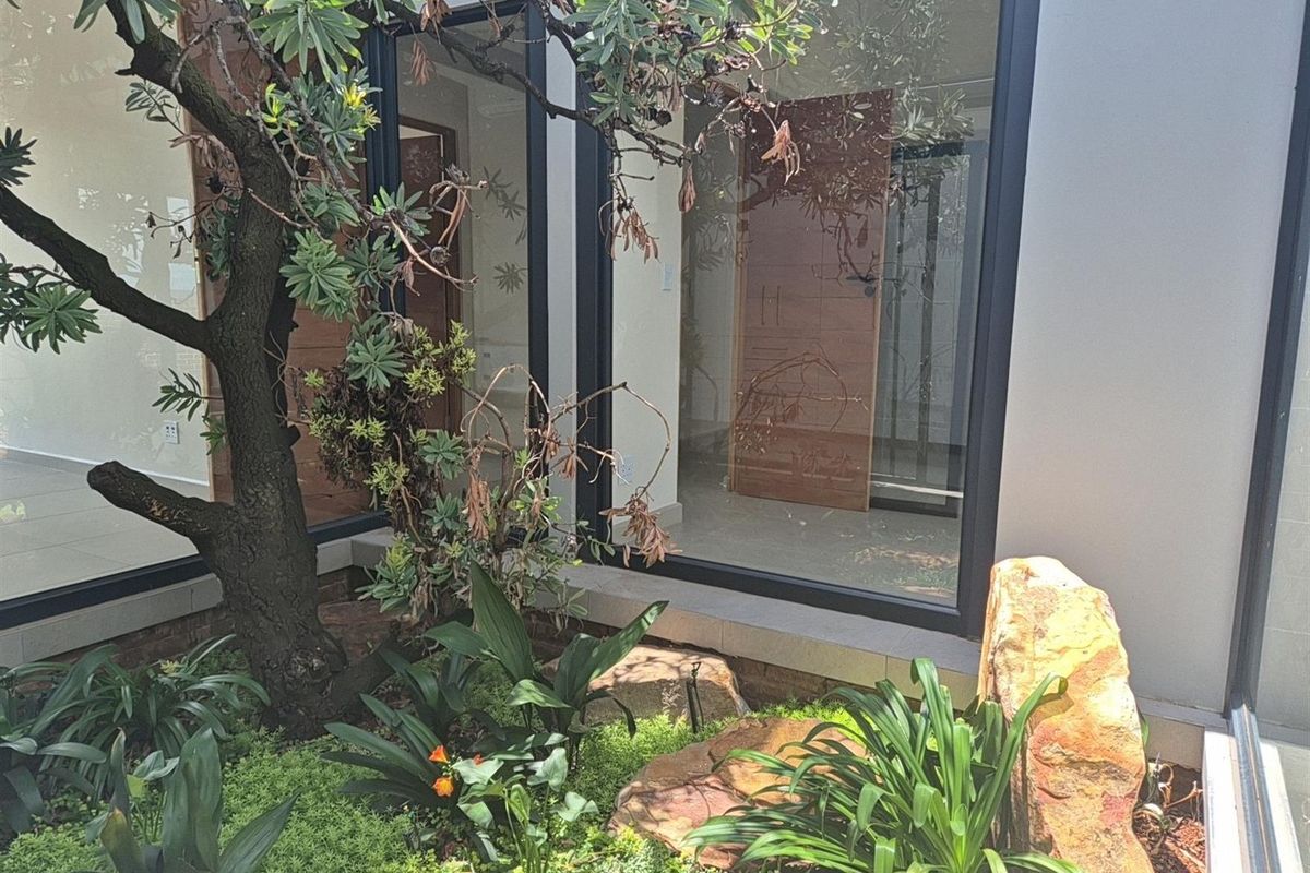 A view of a modern interior space through large floor-to-ceiling glass windows, overlooking a landscaped courtyard garden with mature trees and stone features.