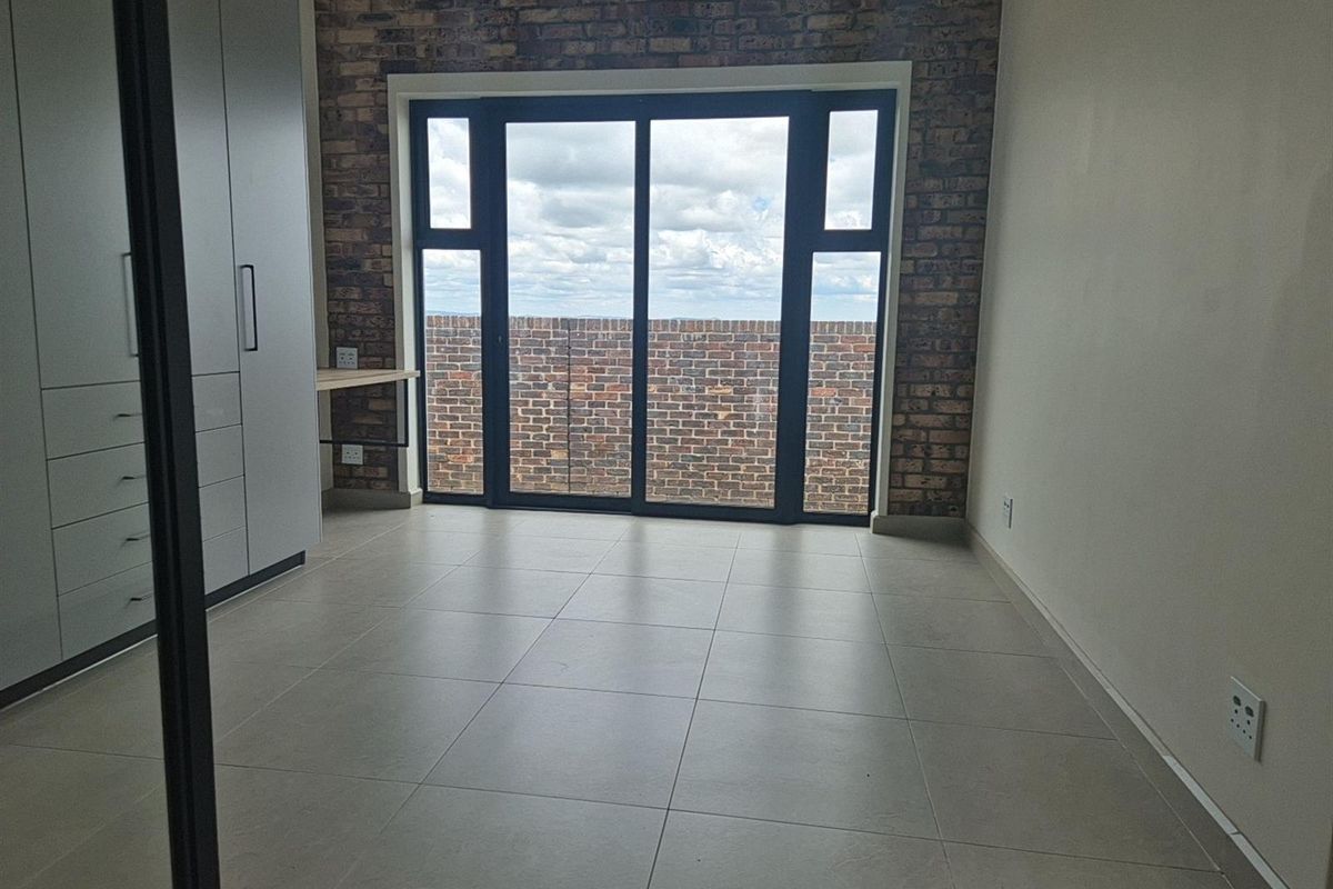 A modern bedroom featuring tiled flooring, built-in cabinetry, and a feature brick wall with sliding glass doors leading to an outdoor area.