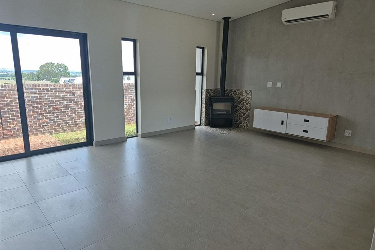 Spacious living area featuring large sliding glass doors, tiled flooring, a modern built-in fireplace with decorative tiling, and a wall-mounted air conditioning unit.