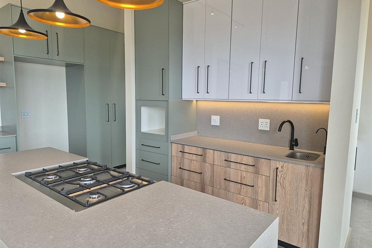 Modern kitchen featuring a central island with a built-in gas hob, stone countertops, two-tone cabinetry, and integrated under-cabinet lighting.