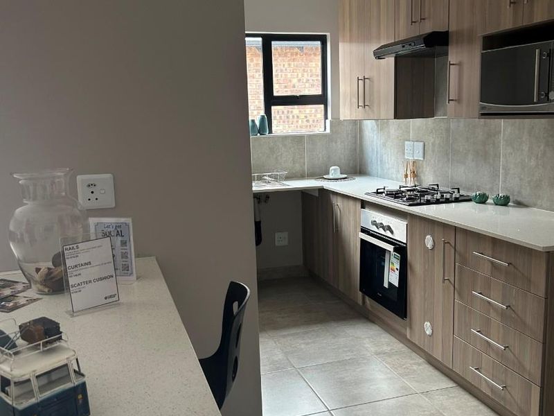 Modern kitchen featuring wood-look cabinetry, stone countertops, built-in oven, gas hob, and extractor fan, with tiled flooring and a breakfast bar.