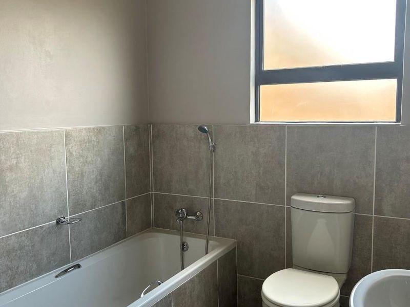 A functional bathroom featuring a built-in bathtub with shower attachment, a standard toilet, and tiled wall finishes.