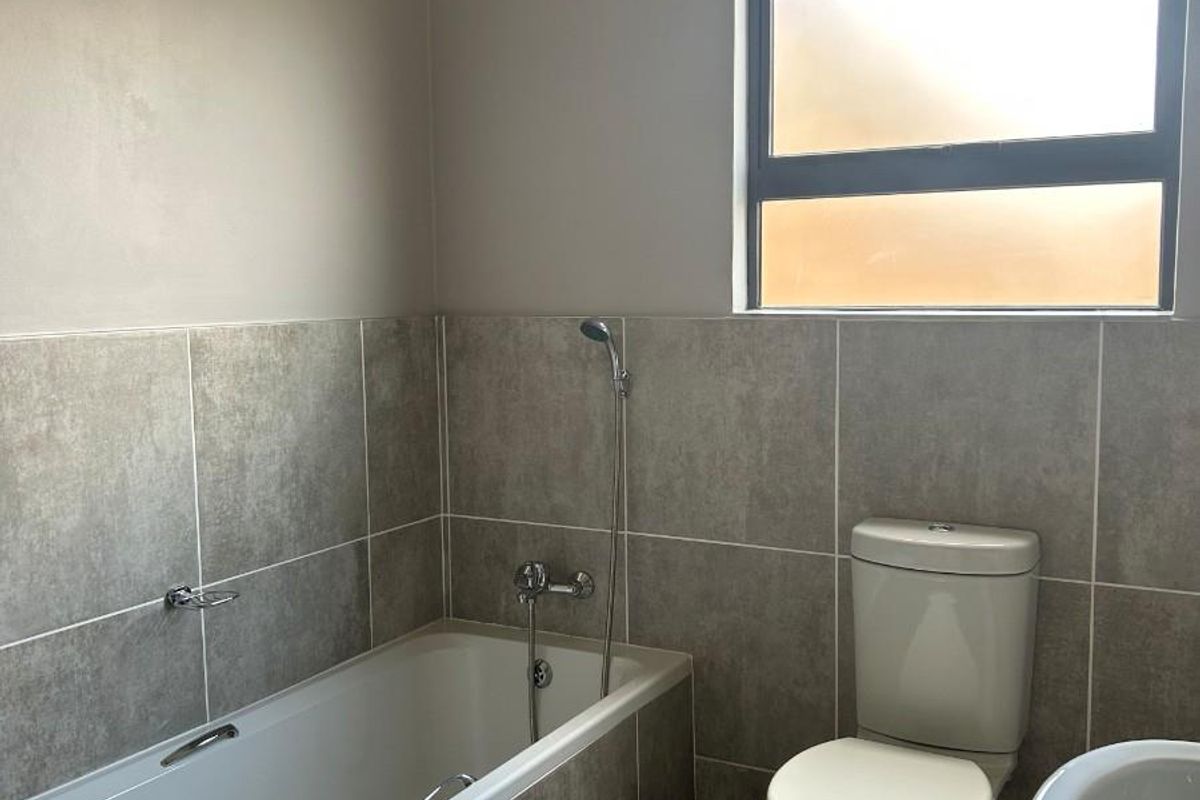 A functional bathroom featuring a built-in bathtub with shower attachment, a standard toilet, and tiled wall finishes.