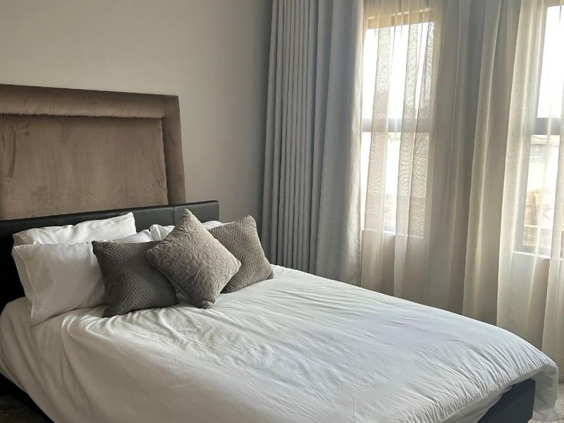 A well-maintained bedroom featuring neutral wall tones, large windows with floor-to-ceiling curtains, and tiled flooring.
