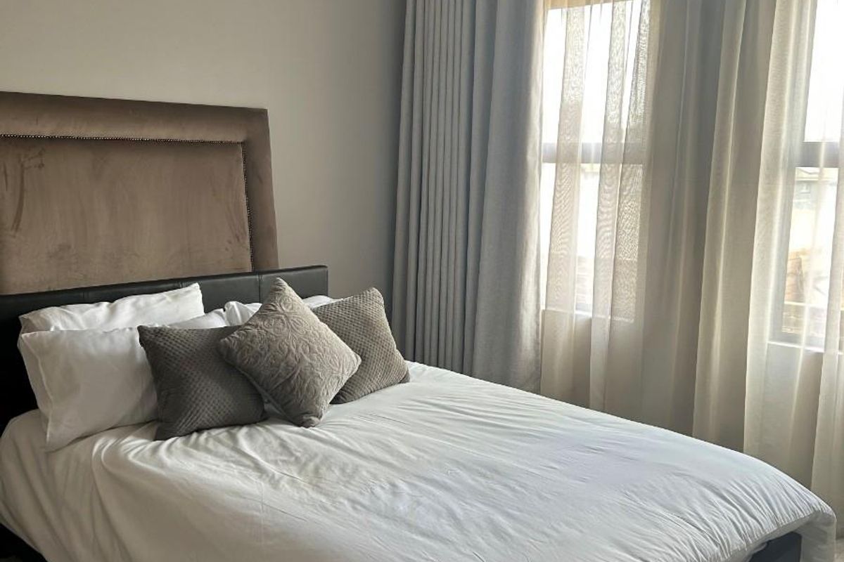 A well-maintained bedroom featuring neutral wall tones, large windows with floor-to-ceiling curtains, and tiled flooring.