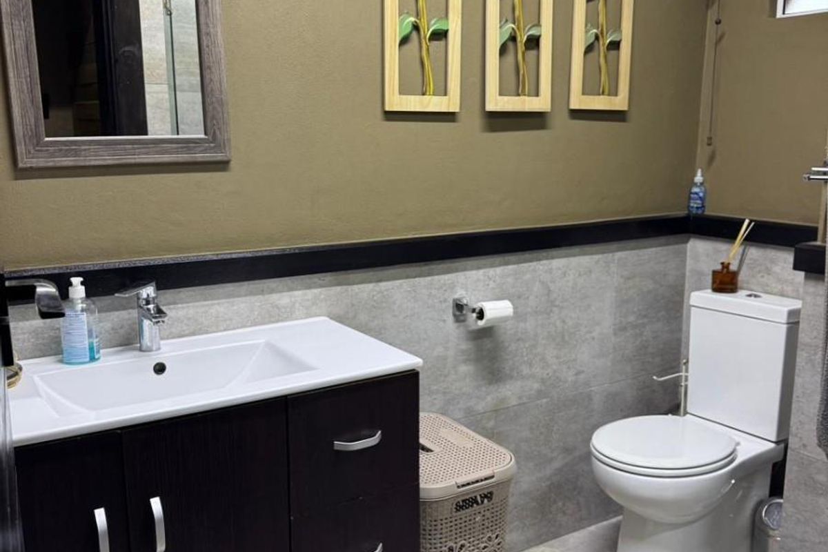 A modern bathroom featuring a dark wood vanity with a white basin, a wall-mounted toilet, and neutral grey wall tiling.