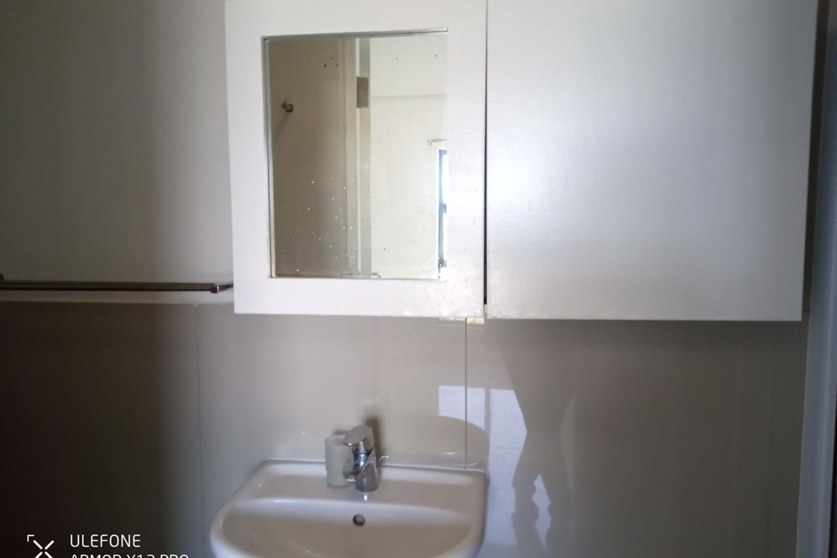 A functional bathroom vanity area featuring a wall-mounted basin, chrome faucet, and a built-in mirrored medicine cabinet with tiled splashback.