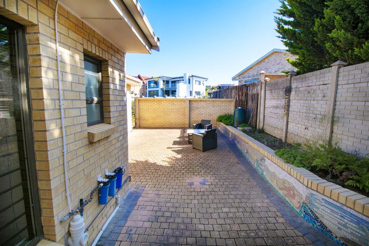 A paved rear courtyard featuring a raised brick garden bed with mosaic detailing and an external water filtration system.