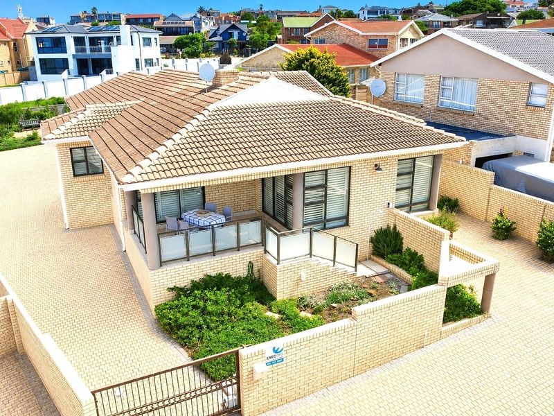 Aerial view of a well-maintained brick house featuring a tiled roof, paved driveway, and a covered patio with glass balustrades.