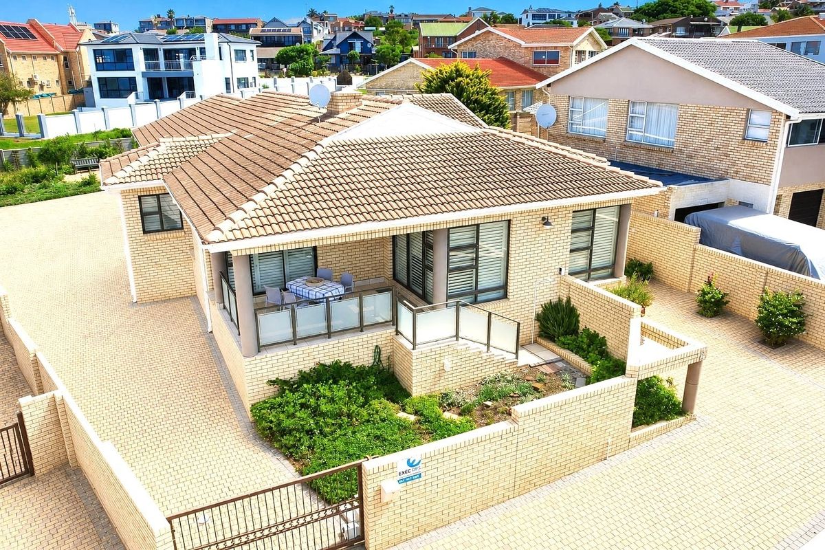 Aerial view of a well-maintained brick house featuring a tiled roof, paved driveway, and a covered patio with glass balustrades.