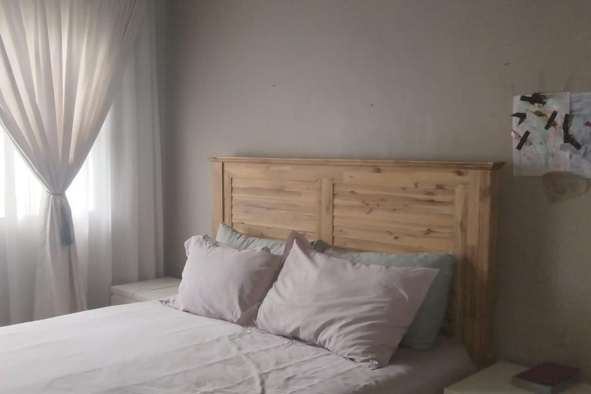 A cozy bedroom featuring a wooden headboard, neutral wall tones, and soft window drapery, providing a comfortable and functional sleeping space.