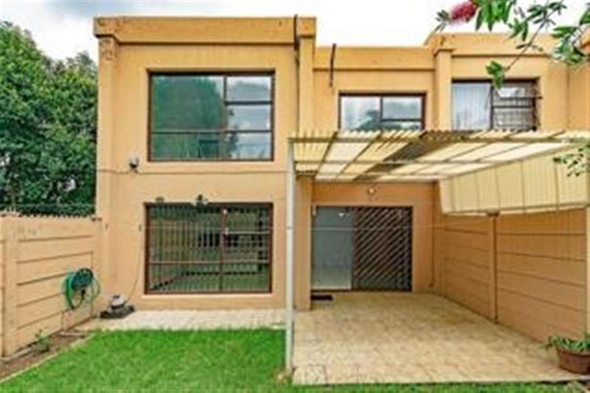 Rear view of the apartment featuring a paved covered patio, sliding glass doors with security bars, and a small private garden area.