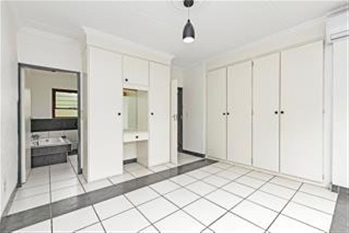 Spacious bedroom featuring extensive built-in cabinetry, a vanity area, tiled flooring, and an integrated air conditioning unit, with an adjoining bathroom.