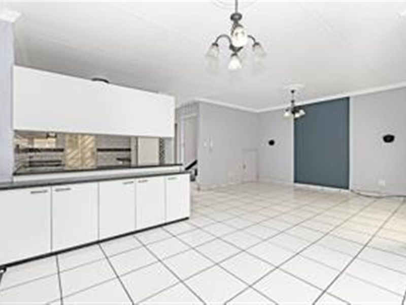 An open-plan living and kitchen area featuring white cabinetry, tiled flooring, and neutral wall finishes in a well-maintained, vacant space.