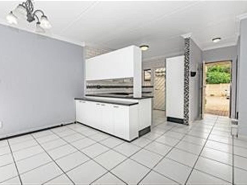 An open-plan living and kitchen area featuring white cabinetry, tiled flooring, and direct access to an outdoor space.