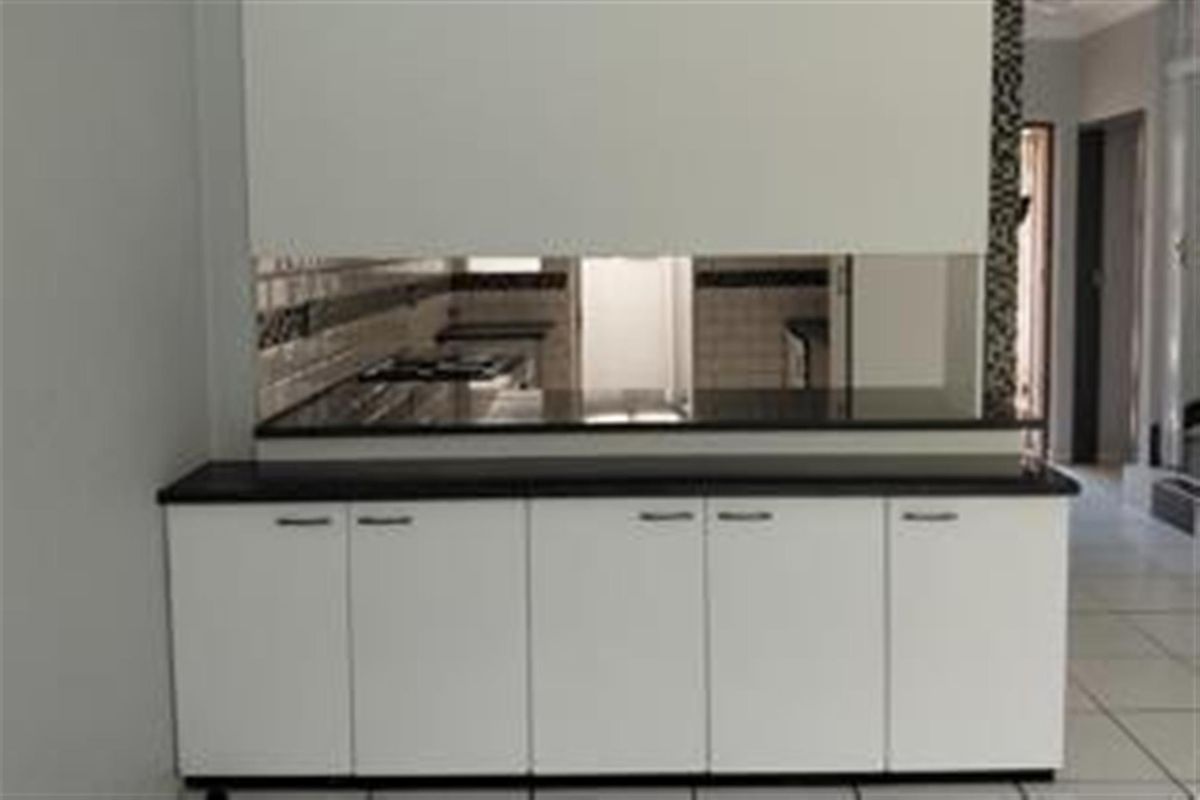 A clean, modern kitchen featuring white built-in cabinetry, dark granite countertops, a tiled backsplash, and a built-in gas hob.