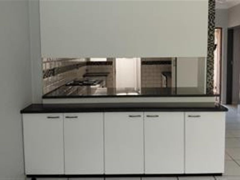 A clean, modern kitchen featuring white built-in cabinetry, dark granite countertops, a tiled backsplash, and a built-in gas hob.