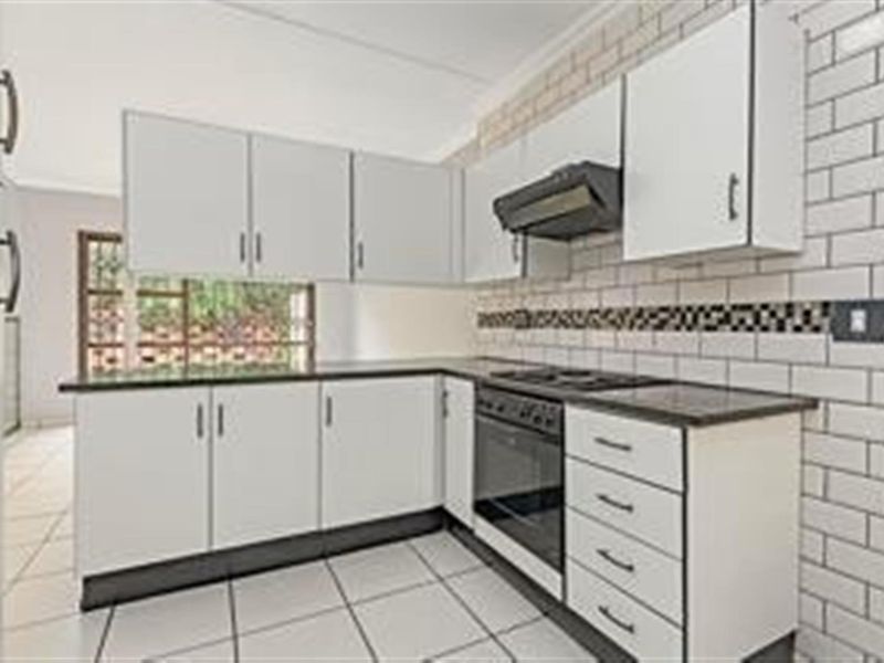 A clean, functional kitchen featuring white cabinetry, dark countertops, a built-in oven with hob, and a classic subway tile backsplash.